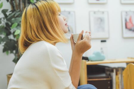 Attractive beautiful asian woman enjoying warm coffee in the kitchen at her home. Asian female wearing comfortable sweater holding a cup of coffee. lifestyle asia woman at home concept.の写真素材