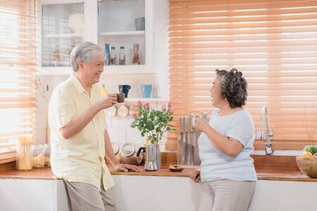 Asian elderly couple drinking warm coffee and talking together in kitchen at home. Chinese couple enjoy love moment while taking together at home. Lifestyle senior family at home concept.の写真素材