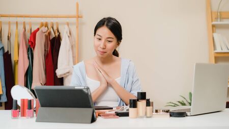 Beauty blogger question and answer by laptop sitting in front tablet for recording video. Happy beautiful young Asian woman use cosmetics review make up tutorial broadcast live video to social networkの写真素材