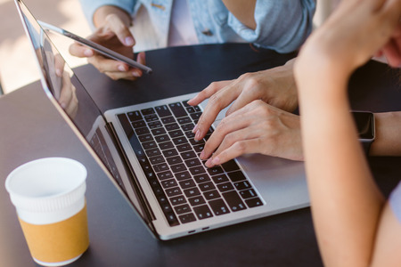 Asian young women working on laptop using and looking smartphone and drinking coffee while sitting in cafe. Lifestyle women communication and working in coffee shop concept.の写真素材