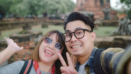 Traveler Asian couple using smartphone taking selfie while spending holiday trip at Ayutthaya, Thailand, Couple enjoy their journey at amazing landmark in traditional city.の写真素材