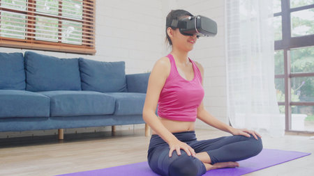 Young Asian teenager woman using virtual reality simulator while practicing yoga in living room,...