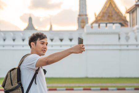 Asian blogger man travel in Bangkok, Thailand, backpacker male using mobile phone make vlog and live in social media while spending sweet time in holiday trip. Lifestyle men travel in city concept.の写真素材