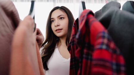 Home wardrobe or clothing shop changing room. Asian young woman choosing her fashion outfit clothes in closet at home or store. Girl think what to wear sweater.の写真素材