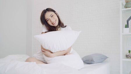 Happy beautiful Asian woman wake up, smiling and stretching her arms in her bed in the bedroom. Young asia female use relax time at home. Lifestyle woman at home concept.の写真素材