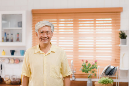 Asian elderly man feeling happy smiling and looking to camera while relax in kitchen at home....