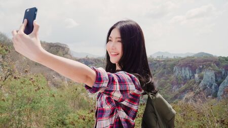 Asian backpacker woman selfie on top of mountain, young female happy using mobile phone taking selfie enjoy holidays on hiking adventure. Lifestyle women travel and relax concept.の写真素材