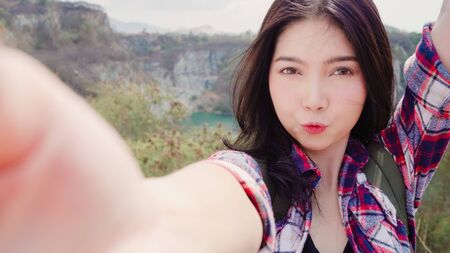 Asian backpacker woman selfie on top of mountain, young female happy using mobile phone taking selfie enjoy holidays on hiking adventure. Lifestyle women travel and relax concept.の写真素材