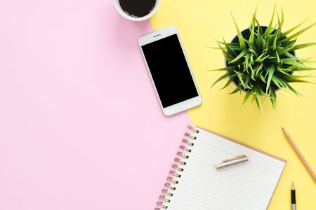 Office desk working space - Flat lay top view of a working space with white blank notebook page, coffee cup and mock up phone on pastel background. Pastel pink yellow color background space concept.の写真素材