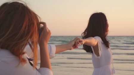 Young Asian lesbian couple using camera taking photo each other near beach. Beautiful women lgbt couple happy romantic moment when sunset in evening. Lifestyle lesbian couple travel on beach concept.の写真素材
