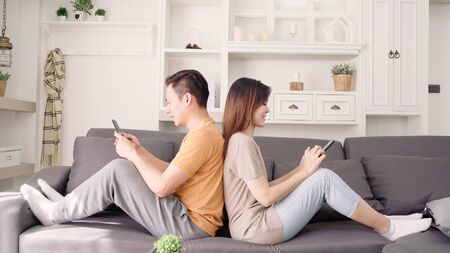 Asian couple using smartphone check social media in living room at home, sweet couple enjoy love moment while lying on the sofa when relax at home. Lifestyle couple relax at home concept.の写真素材