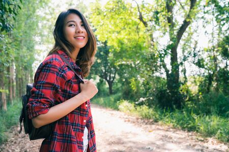 Happy young Asian woman traveler with backpack walking in forest. Hiker Asian woman with backpack walking on path in summer forest. Adventure backpacker travel people concept.の写真素材