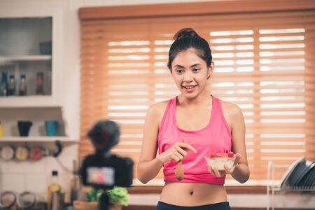 Asian blogger woman make vlog how to diet and lost weight, Young female using camera recording when she eating yogurt in the kitchen. Lifestyle influencer women healthy concept.の写真素材