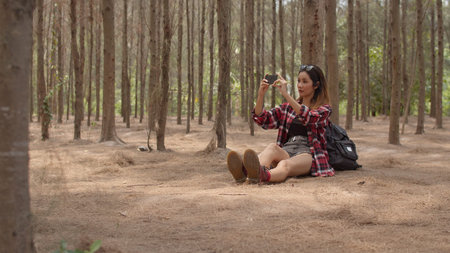Asian hiker woman trekking in forest. Young happy backpack girl using mobile phone take pictures...