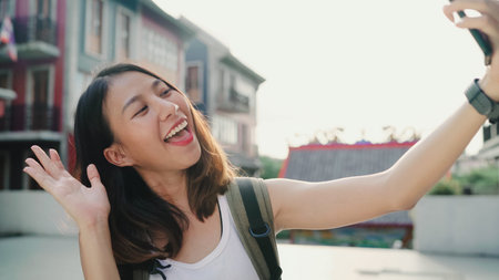 Cheerful beautiful young Asian backpacker blogger woman using smartphone taking selfie while...