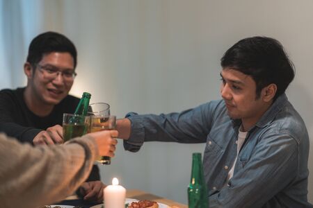 Merry Christmas and Happy New Year! Young friends group having dinner at home. Asian family party with beer and pizza food near christmas tree at house in night. Celebration holiday and togetherness.の写真素材