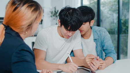Asian Gay lgbtq men couple sign contract on tablet at home, Young couple consulting with real estate financial advisor, Buying new house and handshaking with broker in living room at house concept.の写真素材