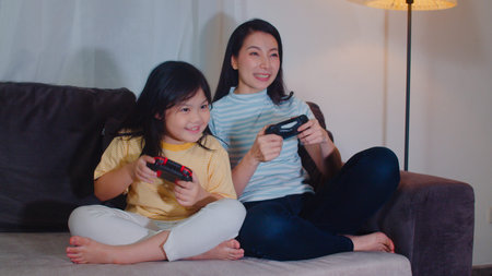 Young Asian family and daughter play games at home in night. Korean mother with little girl using...