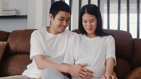 Young Asian Pregnant couple man touch his wife belly talking with his child. Mom and Dad feeling...