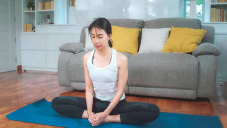 Young Asian woman practicing yoga in living room. Attractive beautiful female working out for healthy at home. Lifestyle woman exercise concept.の写真素材