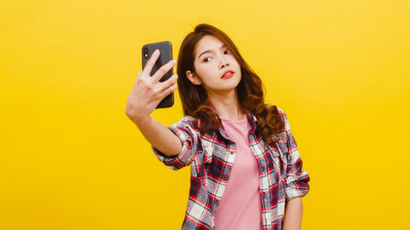 Smiling adorable Asian female making selfie photo on smartphone with positive expression in casual...