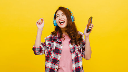 Young Asian lady wearing wireless headphones listening to music from smartphone with cheerful...