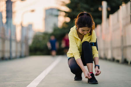 Beautiful young Asia athlete lady exercises tying laces for work out in urban environment. Japanese teen girl wearing sport clothes on walkway bridge in early morning. Lifestyle active sporty in city.の写真素材