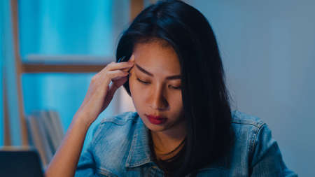 Millennial young Chinese businesswoman working late night stress out with project research problem on laptop in living room at modern home. Asia people occupational burnout syndrome concept.の写真素材