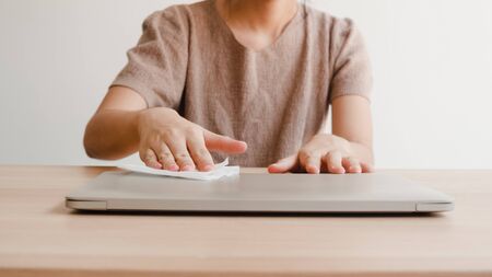 Asian woman using alcohol spray on tissue clean laptop before open for protect coronavirus. Female clean computer for hygiene when social distancing stay at home and self quarantine time.の写真素材