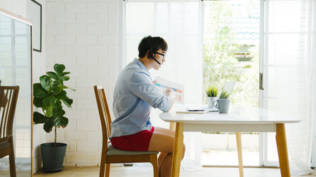 Asia businessman dressed in shirt and shorts use laptop talk to colleagues in video call while work...