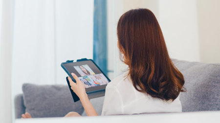 Young Asian business female using tablet video call talking with family while working from home at...