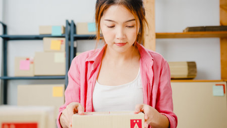 Young Asia entrepreneur businesswoman packing product in cardboard box deliver to customer, working...