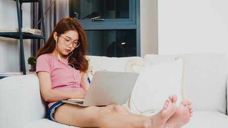 Young Asia teen girl student wears headphones distance learning lesson with online teacher on laptop...