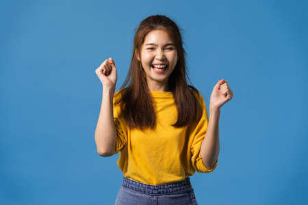 Young Asia lady with positive expression, joyful and exciting, dressed in casual cloth and looking at camera over blue background. Happy adorable glad woman rejoices success. Facial expression conceptの写真素材