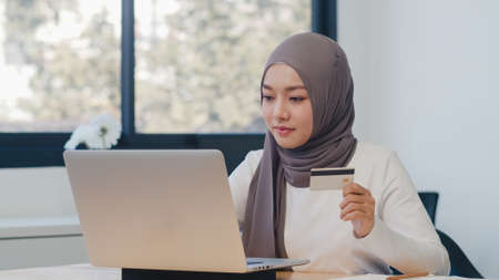 Asia muslim lady using laptop, credit card buy and purchase e-commerce internet in office. Stay at home, online shopping, self isolation, social distancing, quarantine for virus prevention.の写真素材