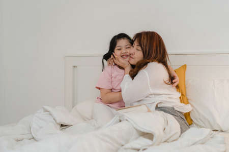 Asian grandmother read fairy tales to granddaughter at home. Senior Chinese, grandma happy relax with young girl enjoy good quality time lying on bed in bedroom at home at night concept.の写真素材