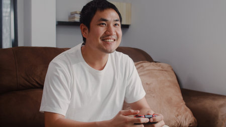 Young Asian man using joystick playing video games in television in living room, male feeling happy using relax time lying on sofa at home. Men play games relax at home concept.の写真素材