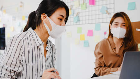Asia businesspeople using computer presentation meeting brainstorming ideas about new project colleagues and wear protective face mask back in new normal office. Lifestyle and work after coronavirus.の写真素材