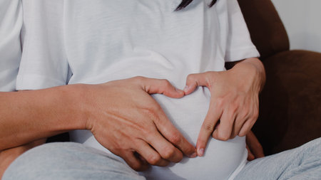 Young Asian Pregnant couple making heart sign holding belly. Mom and Dad feeling happy smiling...