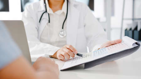 Young Asia female doctor in white medical uniform using clipboard is delivering great news talk discuss results or symptoms with male patient sitting at desk in health clinic or hospital office.の写真素材