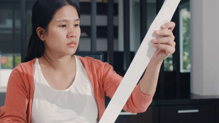 Young Asian Pregnant woman records of income and expenses at home. Mom worried, serious, stress while record budget, tax, financial document working in living room at home concept.の写真素材