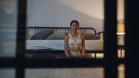 Young Asia lady in sportswear doing yoga exercise working out in living room at home at night.の写真素材