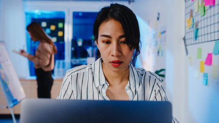 Happy Asia businesswoman social distancing in new normal situation for virus prevention while using laptop online business overtime back at work in office night.の写真素材