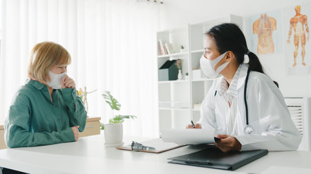 Young Asia lady doctor wear protective mask using clipboard is delivering great news talk discuss results or symptoms with girl patient in hospital office.の写真素材