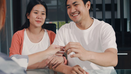 Young Asian Pregnant couple sign contract documents at home, Japanese family consulting with real estate financial advisor, Buying new house and handshaking with broker giving keys in living room.の写真素材