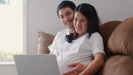 Young Asian Pregnant couple using laptop search pregnancy information. Mom and Dad feeling happy...