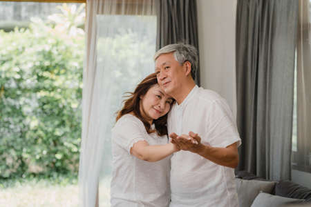 Asian elderly couple dancing together while listen to music in living room at home, sweet couple enjoy love moment while having fun when relaxed at home. Lifestyle senior family relax at home concept.の写真素材