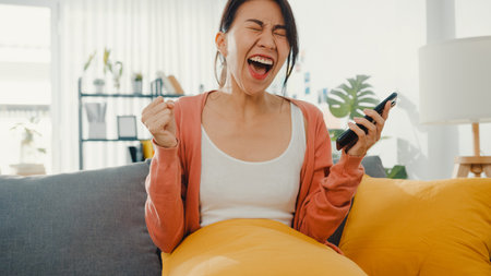 Beautiful asian lady sit on sofa feel exciting with great news at home. Success interview, Graduate achievement, Dating match accept, startup credit approve, Pass Test, Employer accept job concept.の写真素材