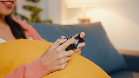 Young Asia lady using wireless controller play video game having funny happy moment on sofa in...