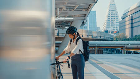Asian businesswoman go to work at office walk and smile wear backpack look around take bicycle on street around building on a city street. Bike commuting, Commute on bike, Business commuter concept.の写真素材